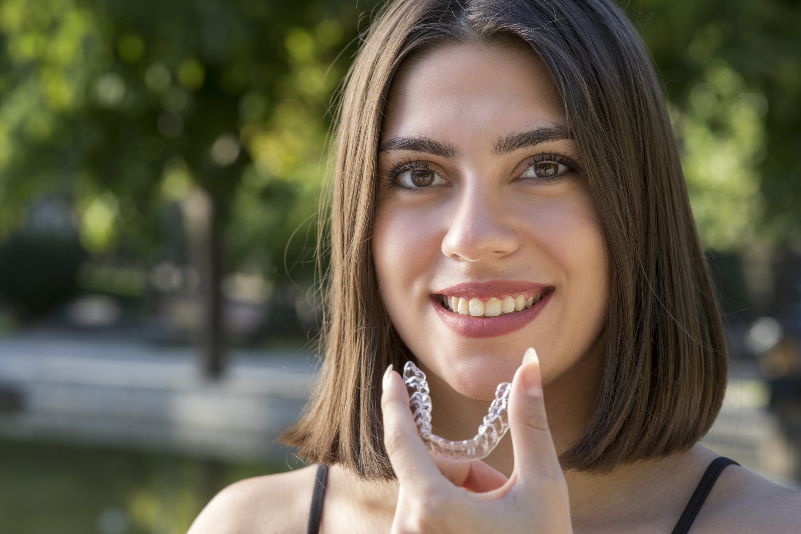 image showing a smiling woman holding invisalign teeth aligners and man in discomfort due to his braces.